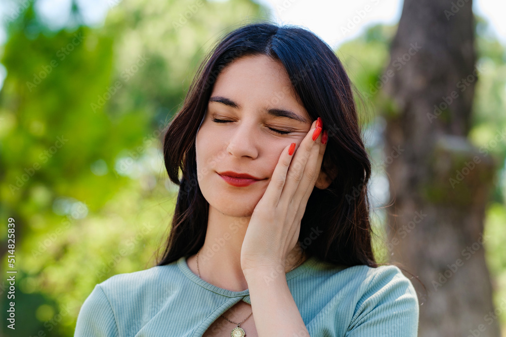 Young brunette woman wearing turquoise tee and orange short on city park, outdoors touching mouth with hand with painful expression because of toothache or dental illness on teeth.