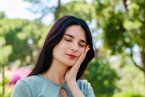 Young caucasian woman wearing tee standing on city park  outdoors touching mouth with hand with painful expression because of toothache or dental illness on teeth. Suffering from sensitive.