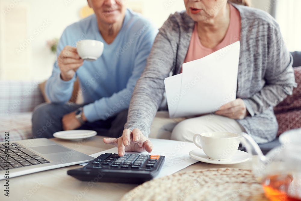 Close-up of married senior couple sitting at coffee table and using calculator while thinking how to save money Close-up of married senior couple sitting at coffee table and using calculator while thinking how to save money