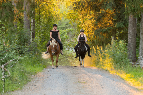 Two riders coming up hill during sunset. The sun is shining from behind. Female riders have have black helmets. © AnttiJussi