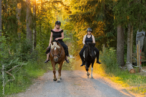 Two riders coming up hill during sunset. The sun is shining from behind. Female riders have have black helmets.