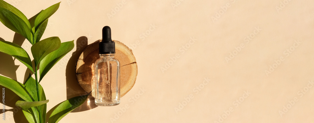 Φωτογραφία Transparent glass dropper bottle with serum, oil, hyaluron on a woodcut in the sunlight with ruscus flower in soft focus
