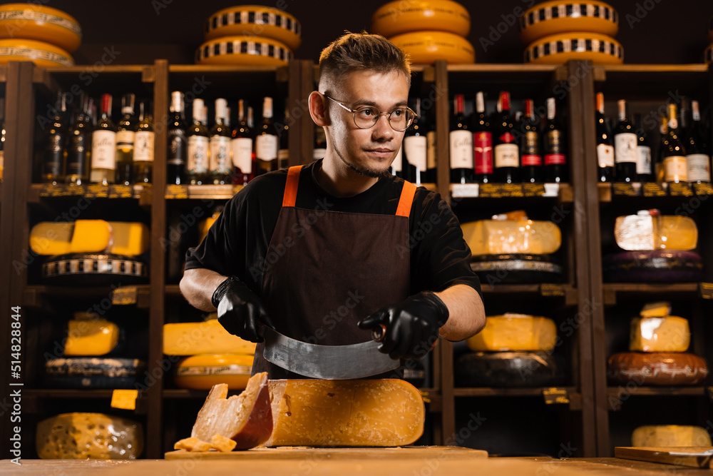 Handsome man worker of cheese shop cut limited gouda with knife. Cheese sommelier working in cheese shop. Creative ideas for advertising cheese products. Handsome man worker of cheese shop cut limited gouda with knife. Cheese sommelier working in cheese shop. Creative ideas for advertising cheese products.