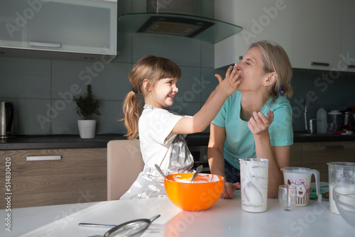 mom and child daughter are cooking pie and having fun in the kitchen. casual lifestyle in real life interior. playful siblings helping to mother. Concept of friendly family. Family spends time togethe