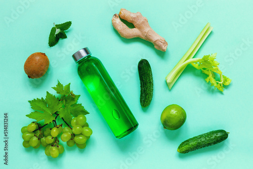 Colorless immunostimulating drink mix in a transparent glass bottle and fresh ingredients fruits and vegetables in green color on a green background photo
