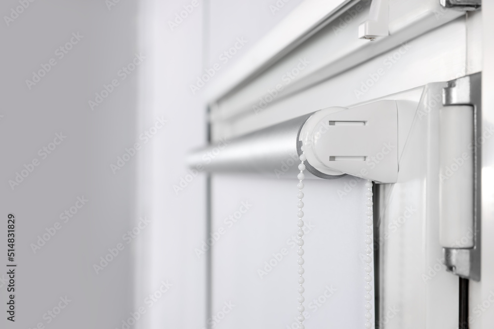 Window with white roller blind indoors, closeup Window with white roller blind indoors, closeup