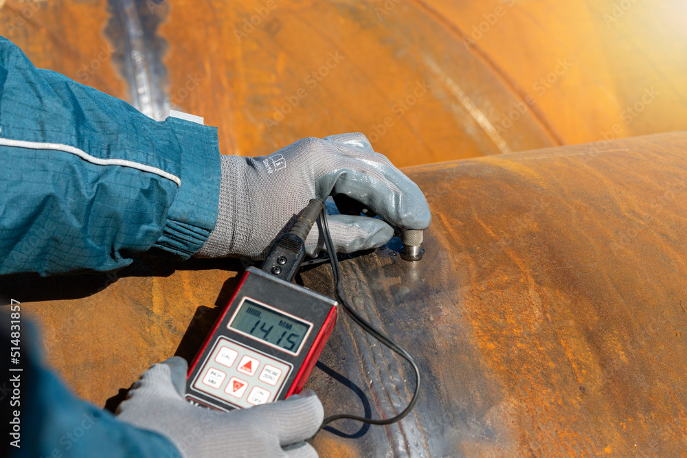 Inspector is measuring thickness of the pipe material from near to weld  with a portable ultrasonic wall thickness measurement gauge. It is a method  of performing non destructive measurement (gauging). Stock Photo