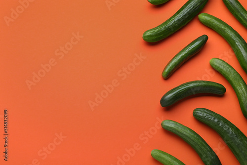 Fresh ripe cucumbers on orange background, flat lay. Space for text photo
