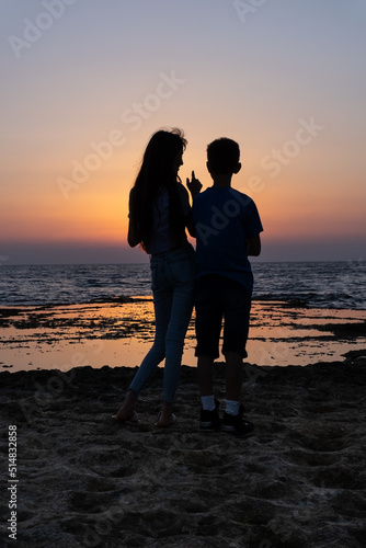 Teenagers, young woman and man speaking and looking at the sunset over the sea in israel. Friendship in childhood silhouette