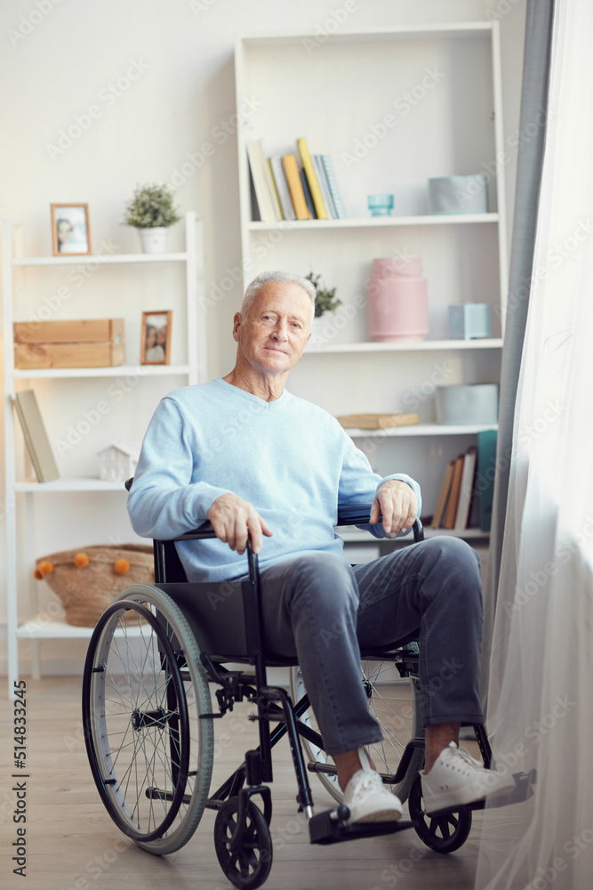 Portrait of content disabled aged man with gray hair sitting in wheelchair in modern room with shelves in background Portrait of content disabled aged man with gray hair sitting in wheelchair in modern room with shelves in background