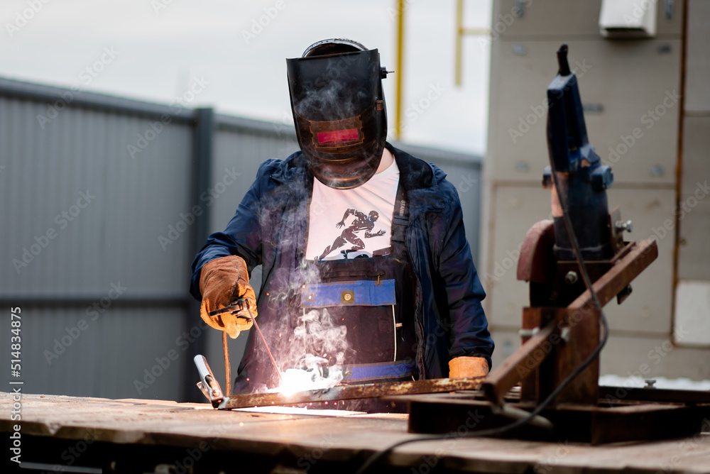 The man works with a welding machine. He is wearing a welder's protective mask and protective gloves. A rare working profession. The man works with a welding machine. He is wearing a welder's protective mask and protective gloves. A rare working profession.