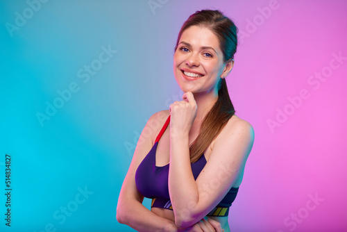 Thinking smiling sporty woman in fitness bra sportswear. Female fitness portrait isolated on neon multicolor background. Girl face with hand touching chin.