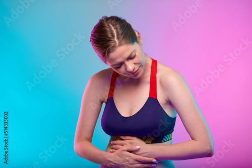 Woman hand on stomach, abdominal pain and digestive disorder. Girl looking down. Female fitness portrait isolated on neon multicolor background. © Yuriy Shevtsov