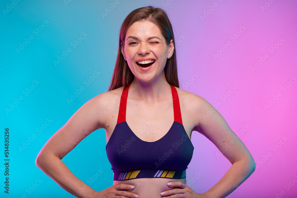 Winking sporty woman in fitness bra sportswear. Female coach fitness portrait isolated on neon multicolor background. Winking sporty woman in fitness bra sportswear. Female coach fitness portrait isolated on neon multicolor background.
