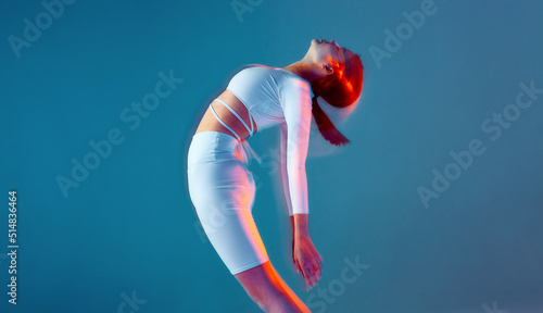 A beautiful girl performs a dance move leaning to the back. A sports model in a white sports outfit on a blue background.
