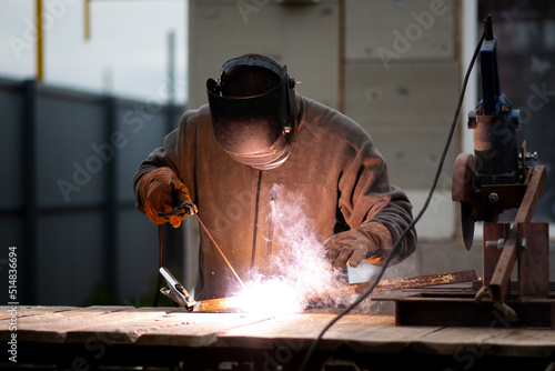 The man works with a welding machine. He is wearing a welder's protective mask and protective gloves. A rare working profession.