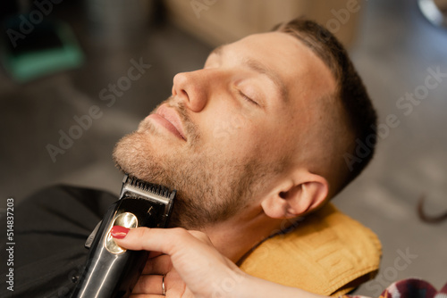 Barbershop, close-up: woman barber shaves mans beard with a razor