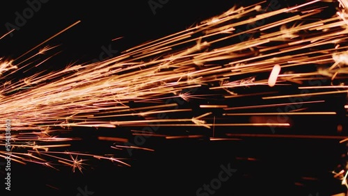 Sparks of angle grinder on black backdrop, closeup. Glowing flow of metal welding spark shining in dark. Industry, tech