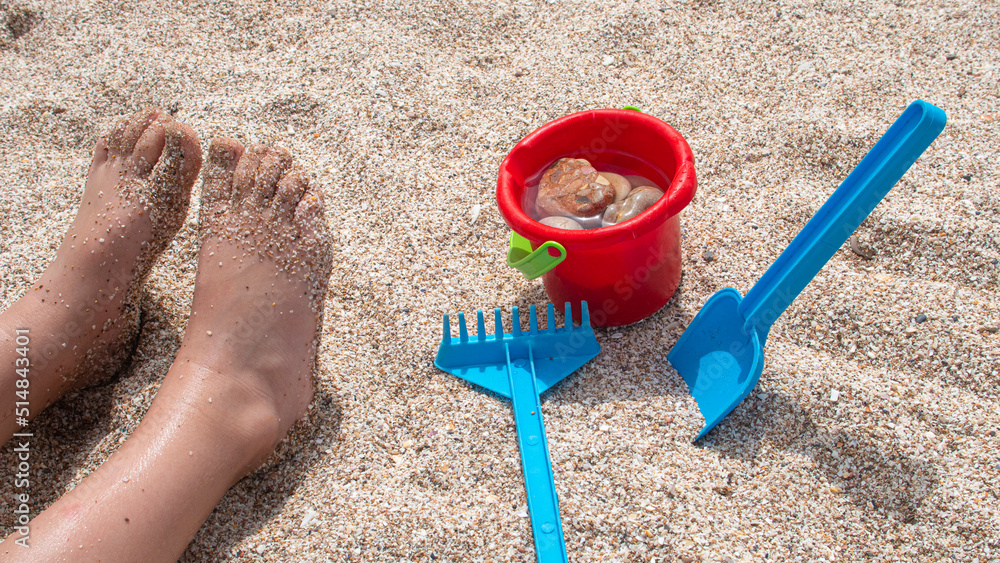 Child's feet full of sand playing with shovels and plastic buckets on the beach Child's feet full of sand playing with shovels and plastic buckets on the beach