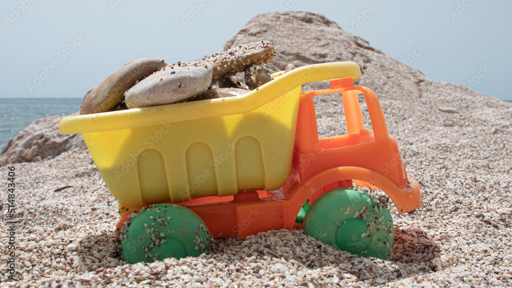 Orange and yellow plastic toy truck loaded with stones on the beach Orange and yellow plastic toy truck loaded with stones on the beach