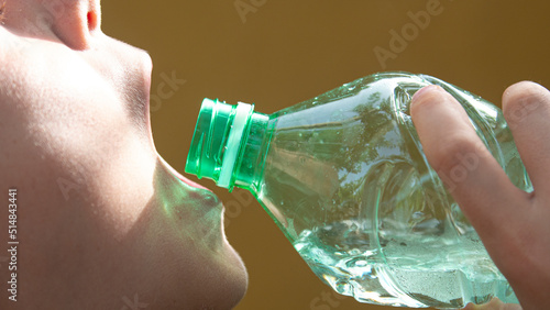Mouth of a ten year old boy drinking water from a transparent plastic bottle