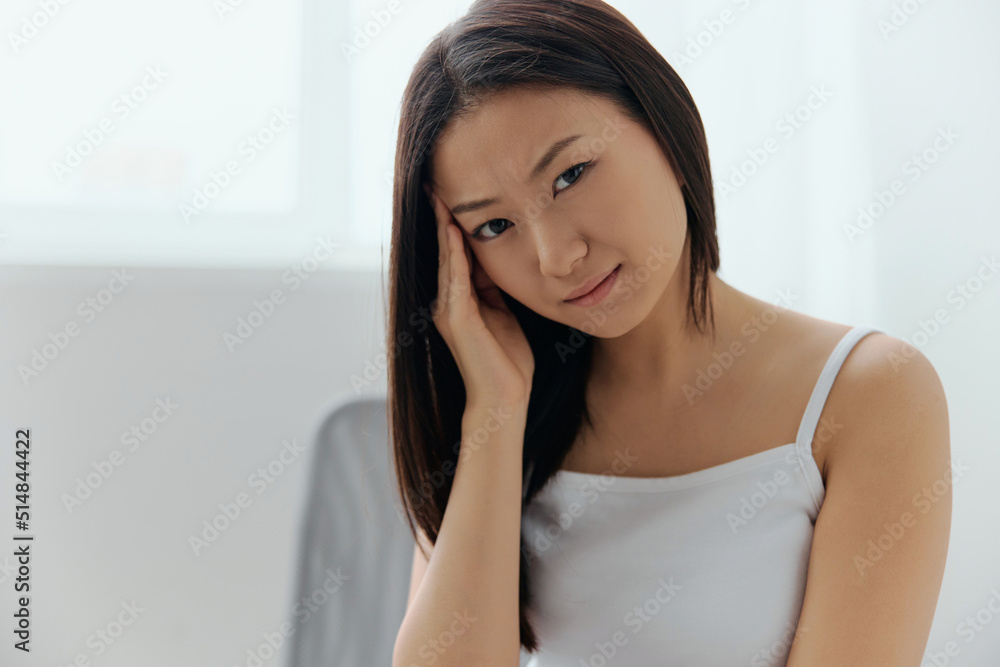 Migraine. Portrait of unhappy suffering from headache tanned beautiful young Asian woman touching forehead at home interior living room. Injuries Poor health Illness concept. Cool offer Banner