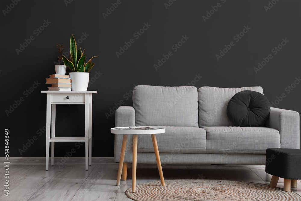 Interior of living room with grey sofa, table and pouf near black wall ...