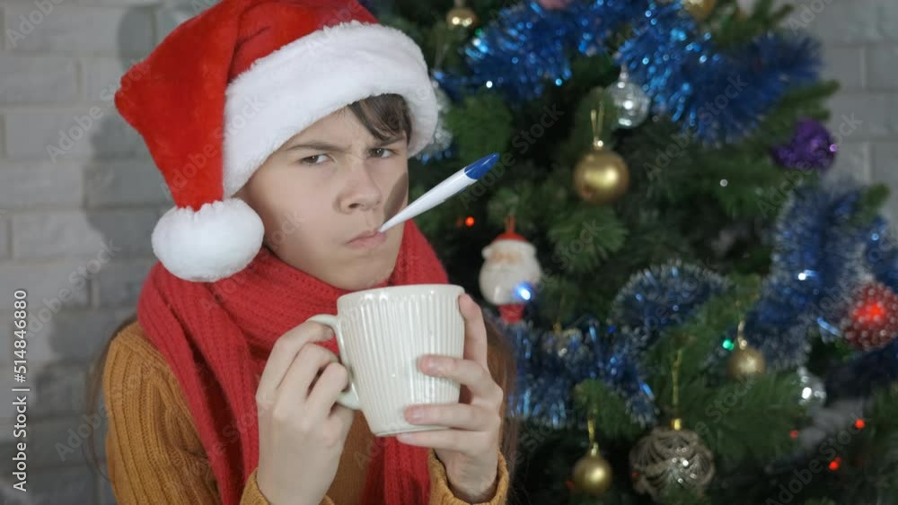 Ill girl with temperature at Christmas. A sick young girl with temperature pas her time with a mug of coffee by the Christmas tree. Ill girl with temperature at Christmas. A sick young girl with temperature pas her time with a mug of coffee by the Christmas tree.