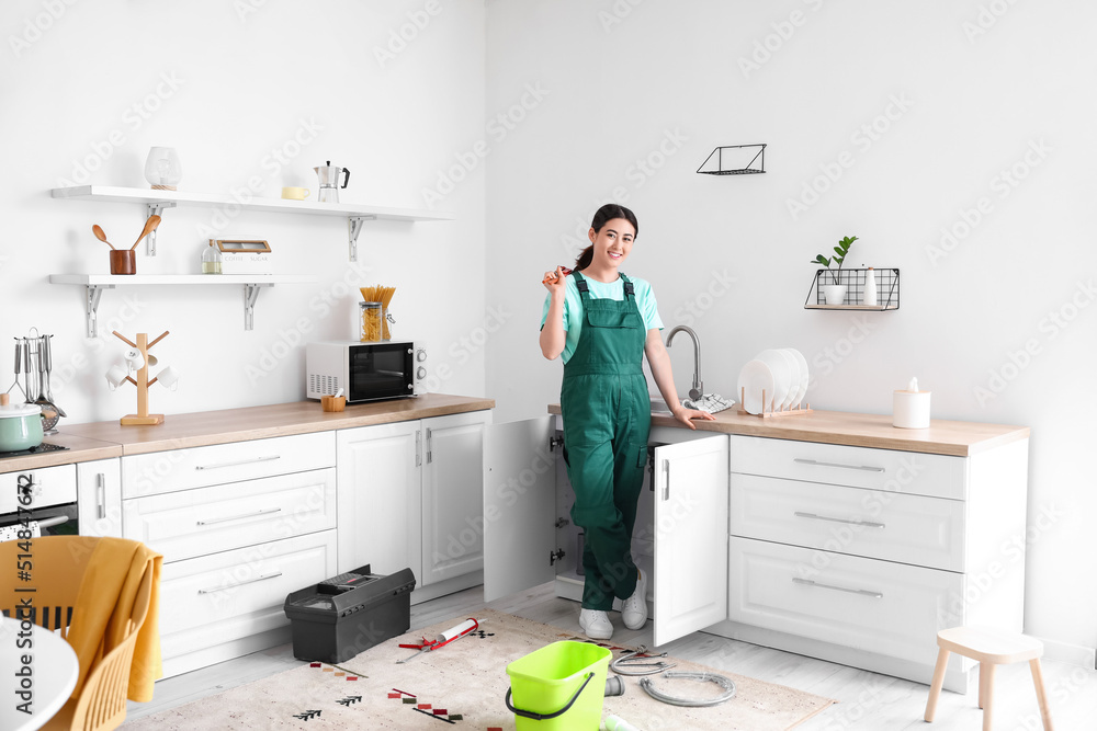 Asian female plumber with pipe wrench near sink in kitchen