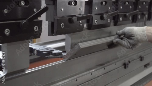 A man working with sheet metal on a CNC hydraulic press brake. He puts the part and bends it into a large machine at an angle.