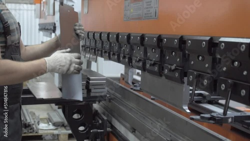A man working with sheet metal on a CNC hydraulic press brake. He puts the part and bends it into a large machine at an angle.