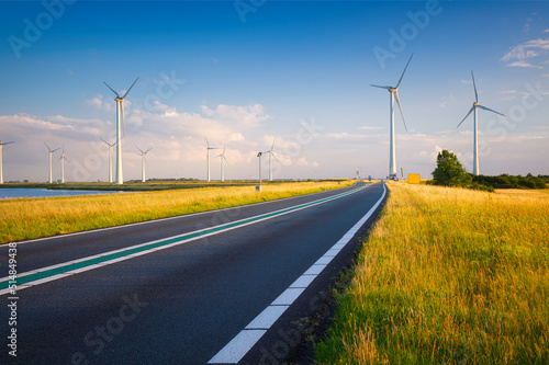 Landscape during sunset with road, field and wind turbines. Windmills for energy production. Green energy in the Netherlands. A beautiful asphalt road with wind power turbines during sunset.