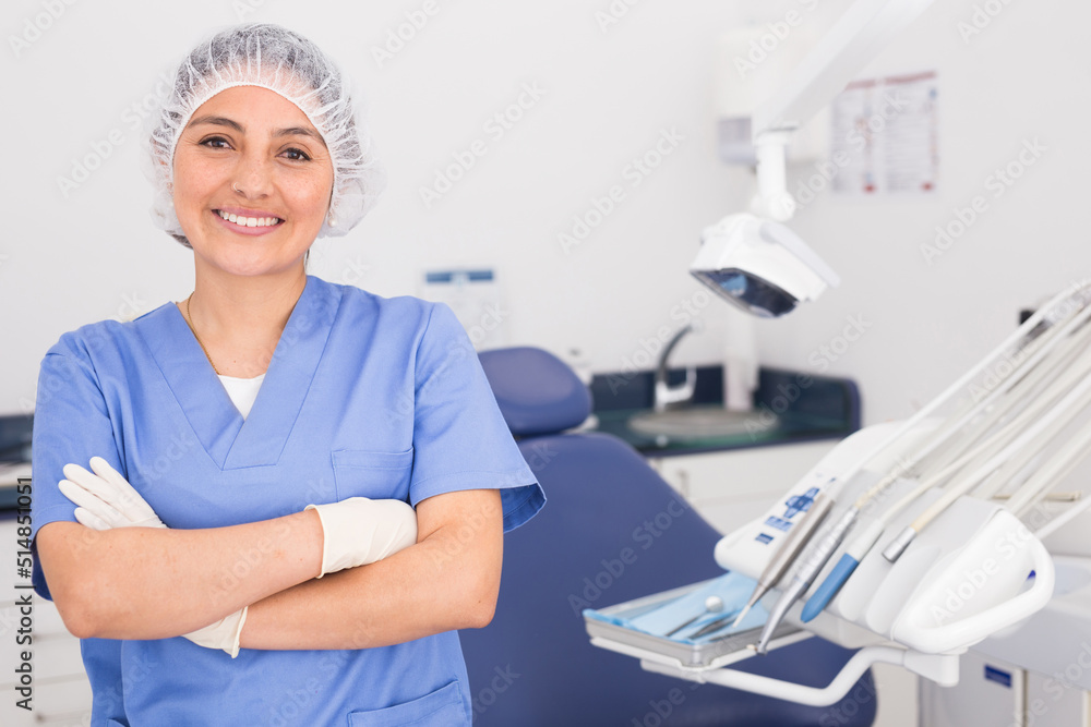 Obraz premium Portrait of a positive young female dentist in uniform with crossed hands at the dental office