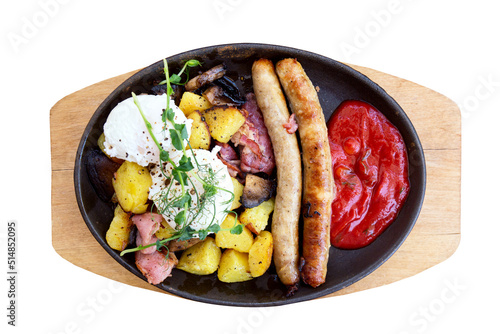 Sausages, potatoes and bacon with a ketchup in frying pan on a board isolated on white background.