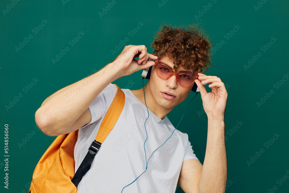a joyful man, a teenager, stands on a green background listening to music with headphones with pink glasses on his face and looks at the camera, holding them on his face a joyful man, a teenager, stands on a green background listening to music with headphones with pink glasses on his face and looks at the camera, holding them on his face