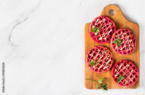 Small round beetroot waffles, on a wooden board. Light background. Top view. Copy space