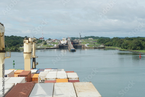Fototapeta Naklejka Na Ścianę i Meble -  Container vessel with cranes approaching Gatun locks in Panama Canal form Atlantic Ocean to pass and reach Pacific Ocean. In the locks are other ships and tugs.