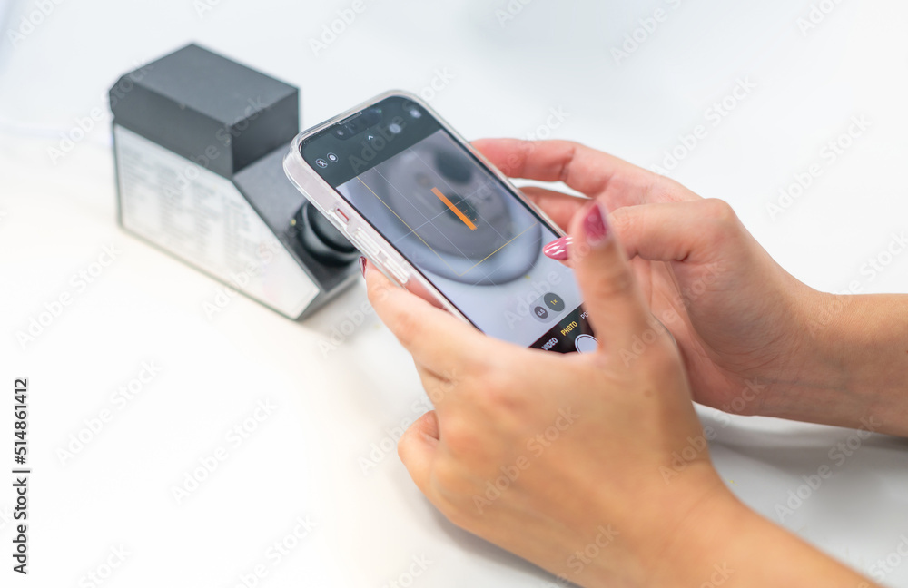 Female hand holding smartphone for taking photo with the RI of refractometer for confirm the type of jewelry. Female hand holding smartphone for taking photo with the RI of refractometer for confirm the type of jewelry.