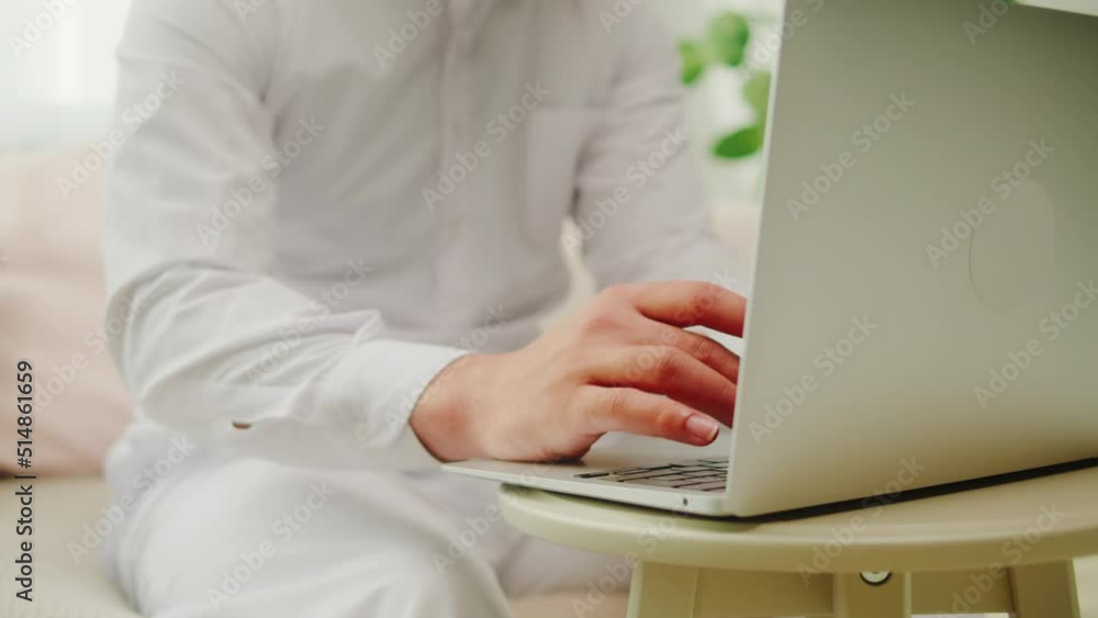 Middle eastern man using laptop. Male person texting at computer keyboard in living room. Wearing traditional Islamic clothes, relaxing at home. Communicating with family and friends online. Middle eastern man using laptop. Male person texting at computer keyboard in living room. Wearing traditional Islamic clothes, relaxing at home. Communicating with family and friends online.