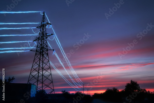 Electricity transmission towers with glowing wires against the sunset sky background.