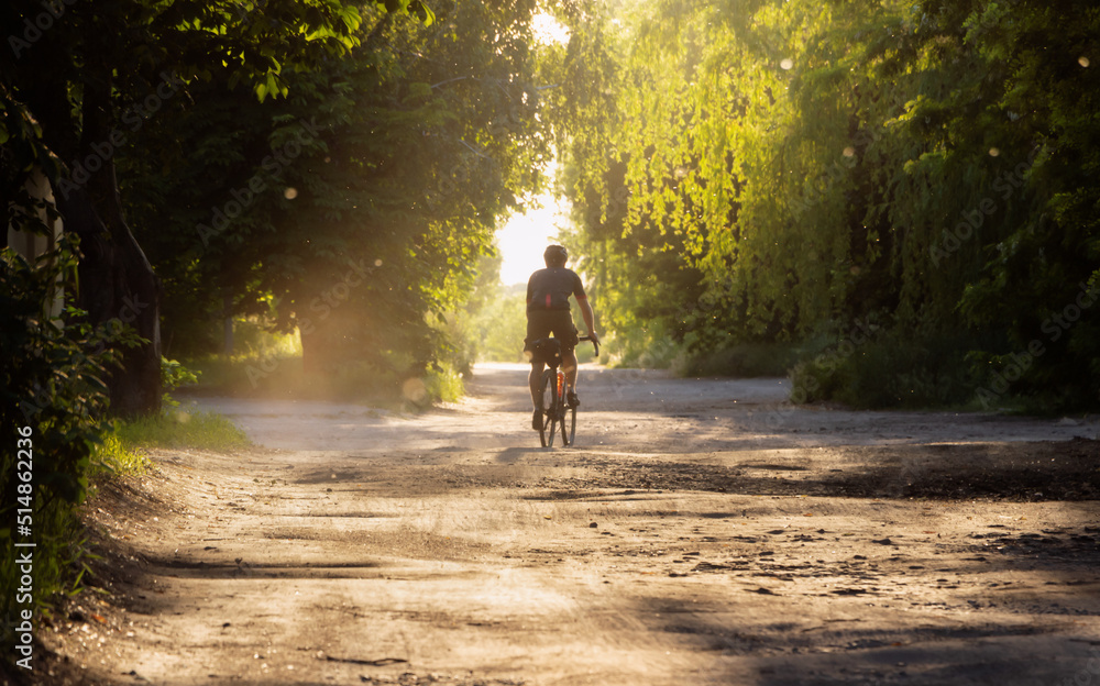 Cyclist rides bicycle on a gravel road at sunset. Soft focus.