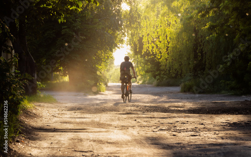 Cyclist rides bicycle on a gravel road at sunset. Soft focus.