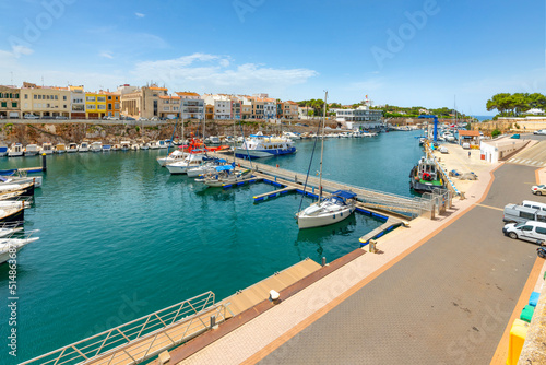 Boats line the picturesque marina port harbor at Ciutadella de Menorca, Spain, a small Balearic island in the Mediterranean Sea, with the colorful village in view.