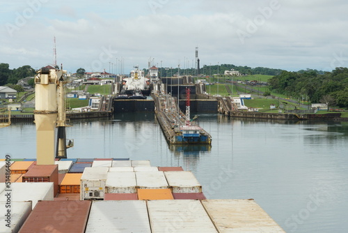 Container vessel with cranes approaching form Atlantic Ocean Gatun locks in Panama Canal to pass and reach Pacific Ocean. In the locks are other ships and tugs.