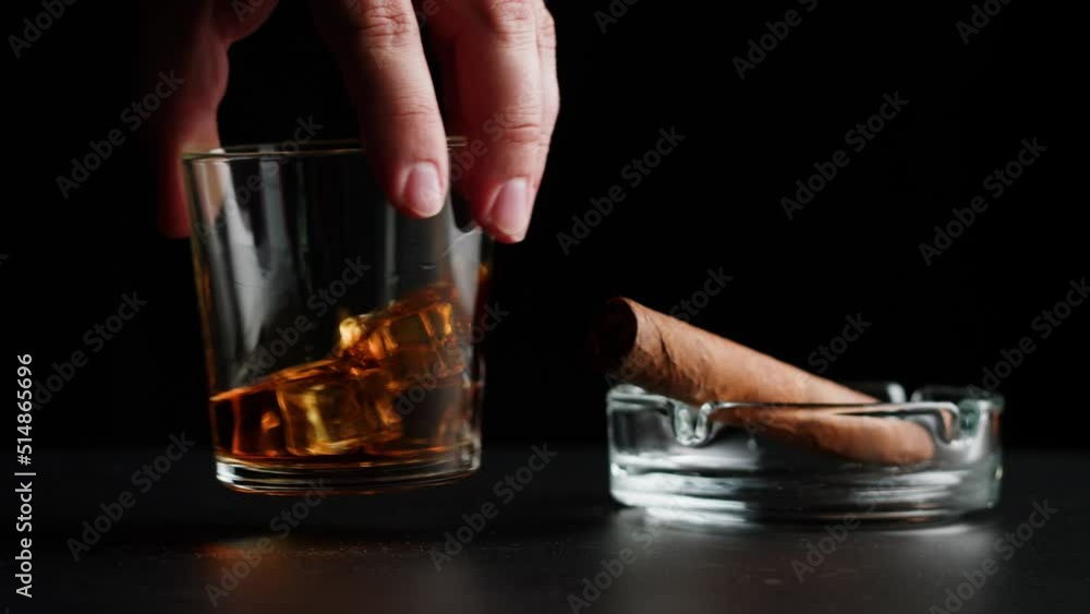 Brandy or whiskey and cigar close-up. Luxury cognac with ice on black background. Alcohol amber drink, drinking rum, liqour beverage in glass. Brandy or whiskey and cigar close-up. Luxury cognac with ice on black background. Alcohol amber drink, drinking rum, liqour beverage in glass.