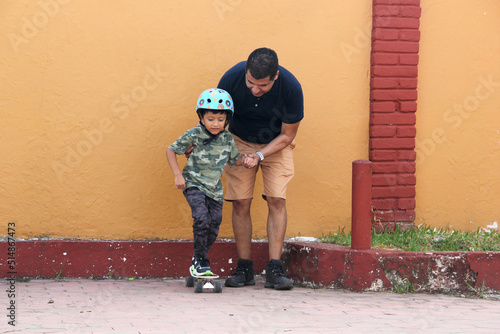 Latin single dad teaches his son to ride a skateboard with a helmet very funny and happy of the achievement of learning something new 