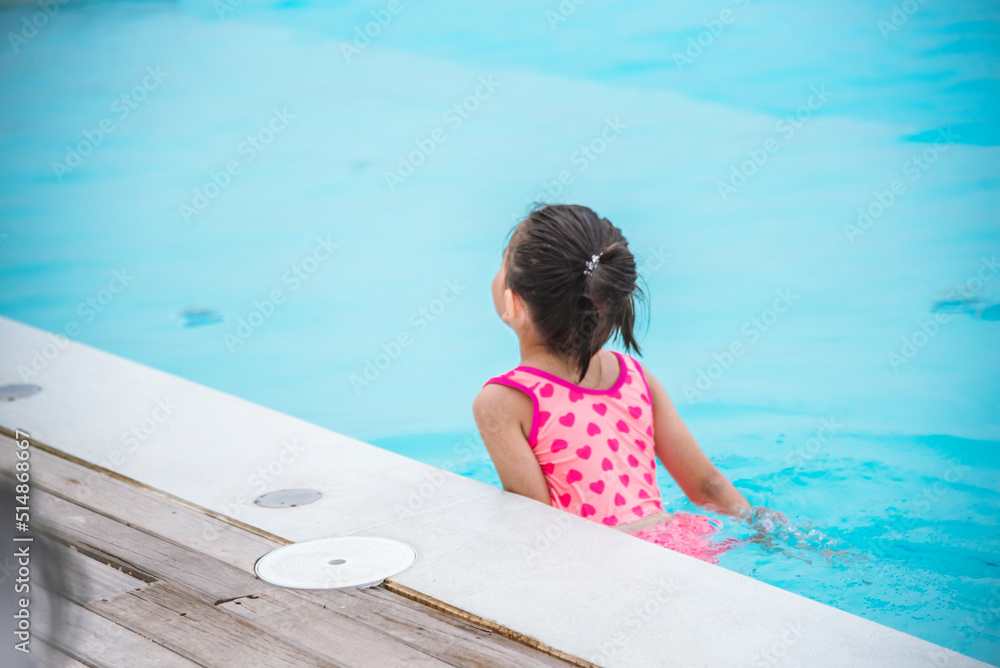 Toddler girl have fun swimming pool summer time with swimwear in blue water at hotel swimming pool outdoor. Kid swim playful water splash with happiness on summer vacation. Happy girl swim concept