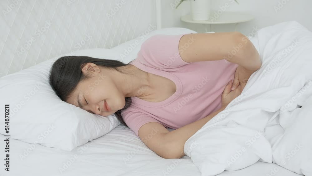 Young asian woman lying on bed pain stomach or bowel with disease constipation or indigestion in the bedroom at home, unhappy female sick and menstruation and stomachache, medical and health concept. Young asian woman lying on bed pain stomach or bowel with disease constipation or indigestion in the bedroom at home, unhappy female sick and menstruation and stomachache, medical and health concept.
