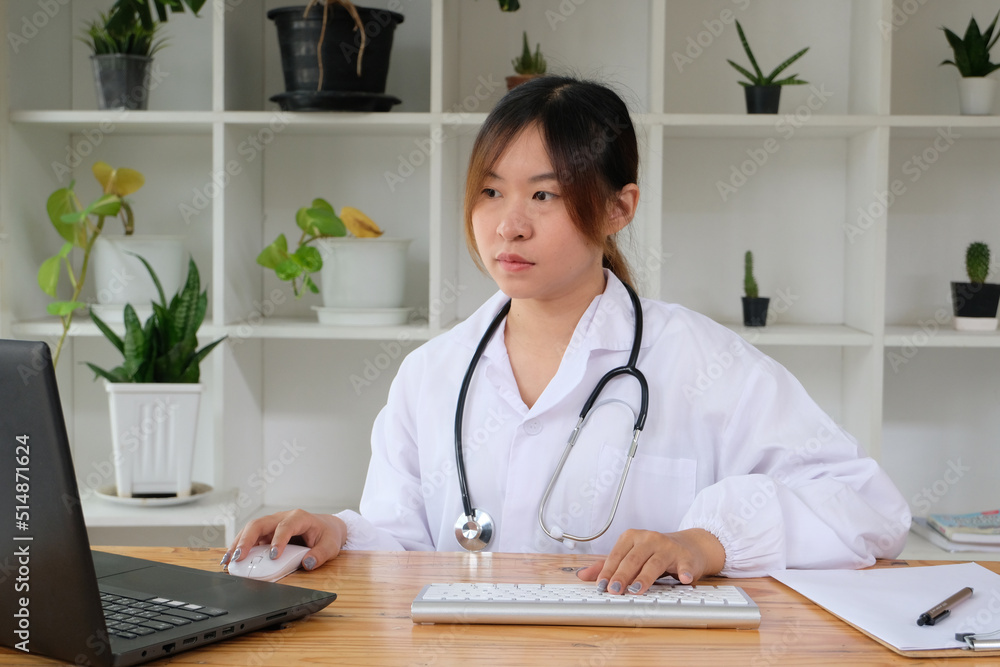 Doctor wearing a stethoscope sitting in a office writing a prescription while sitting at her desk. Smiling female or physician writing in medical file in clinic