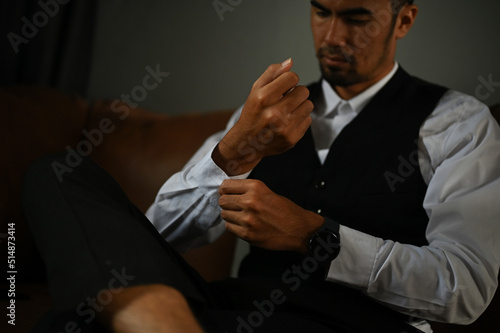 Professional Asian businessman sits on leather sofa, adjusting his cufflinks. cropped © bongkarn